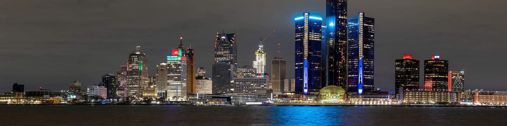 A city skyline at night with illuminated buildings and a river in the foreground.