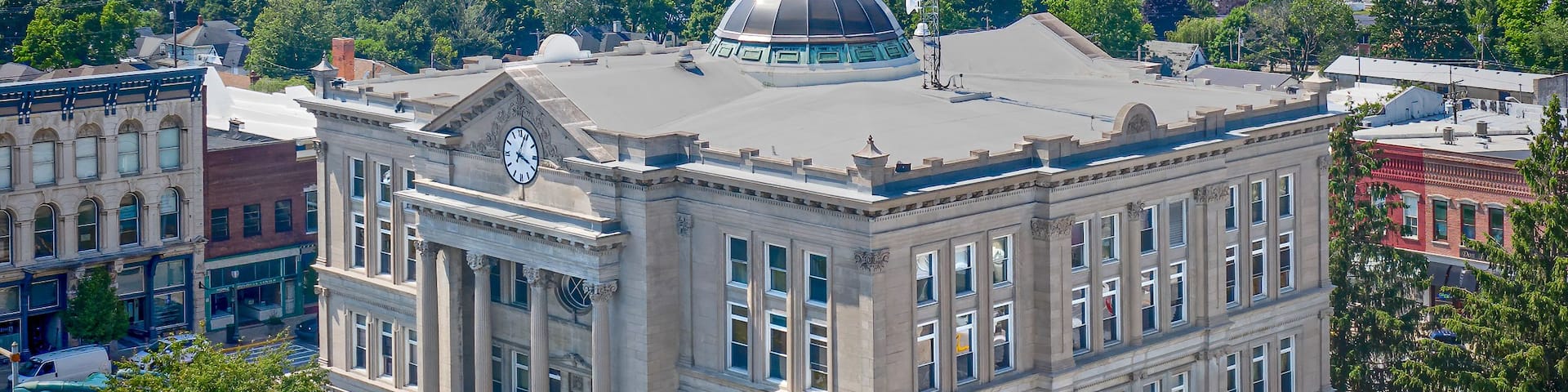 A historic building with a clock tower and a dome, surrounded by lush greenery and a clear sky.