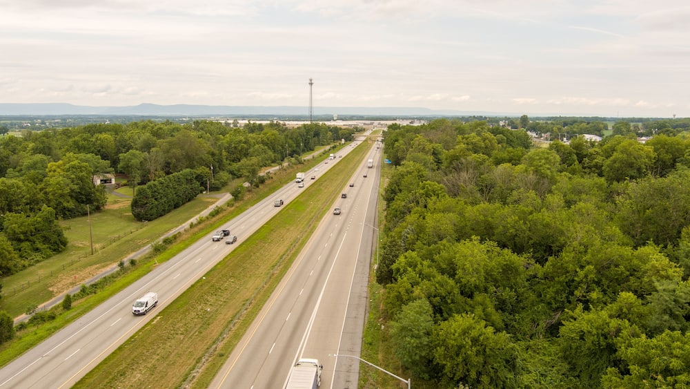 A highway with multiple lanes, surrounded by dense green trees and a distant view of mountains.
