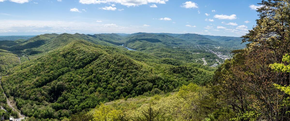A mountainous landscape with dense forests, a winding road, and a small settlement.