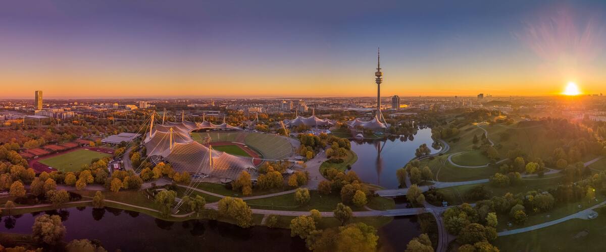 A cityscape at sunset with a prominent tower, a stadium, and a lake.