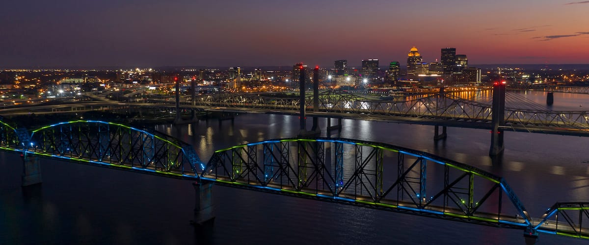 A nighttime cityscape with a brightly lit bridge and a skyline featuring a prominent dome-shaped building.