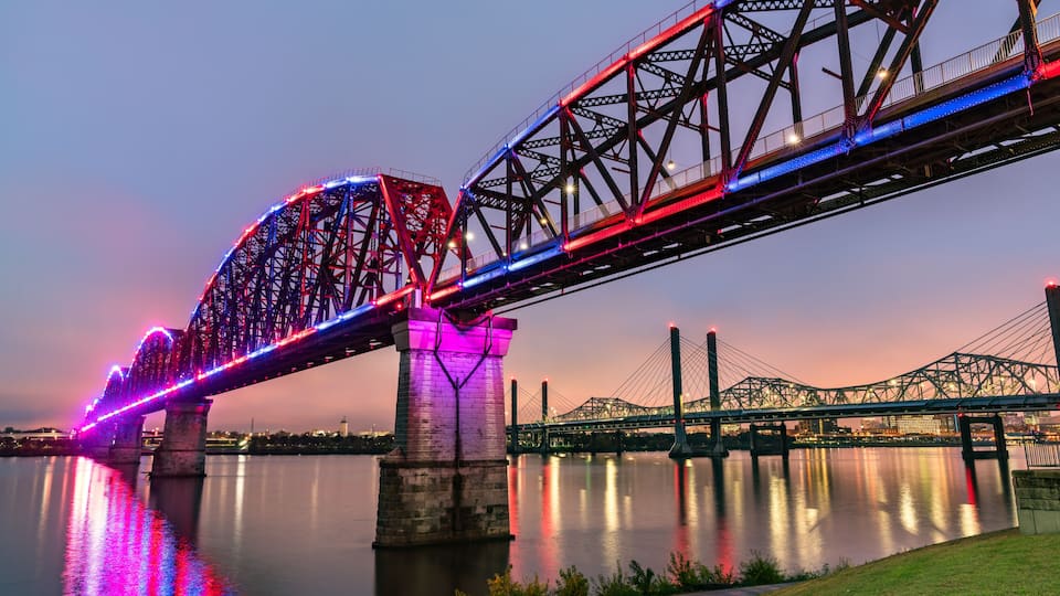 A bridge with colorful lights reflecting on the water at dusk.