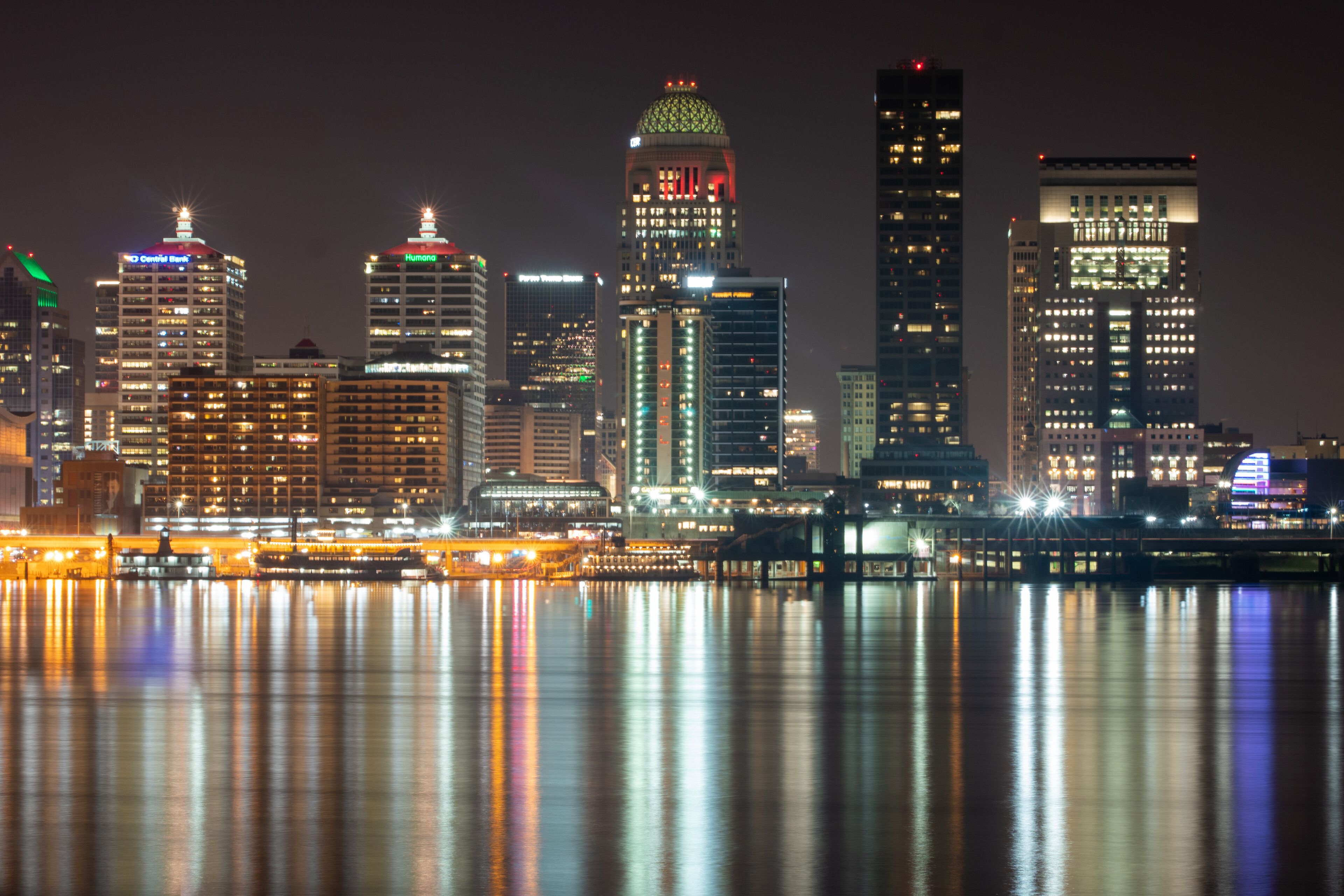 A city skyline at night with illuminated buildings reflecting on the water.