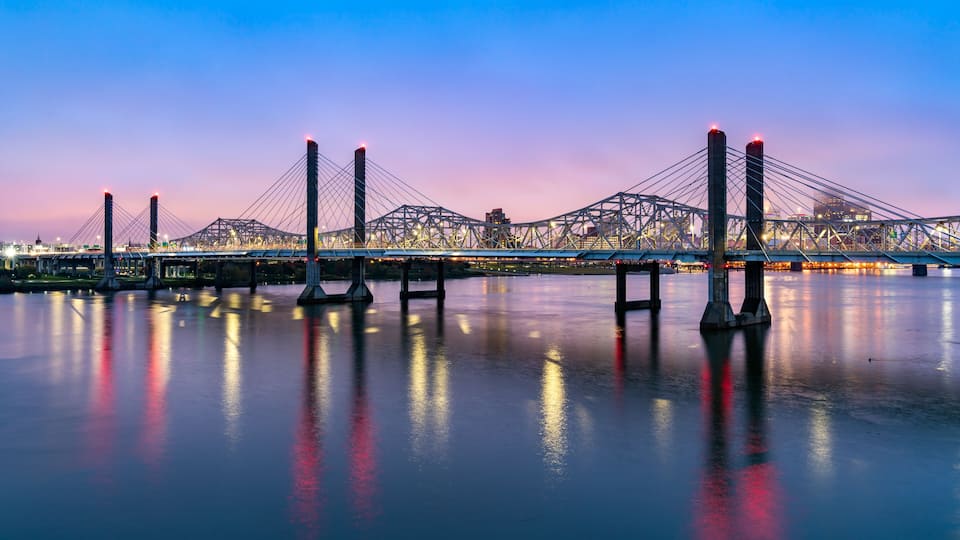 A bridge with multiple towers and cables, spanning over a body of water with city lights in the background.