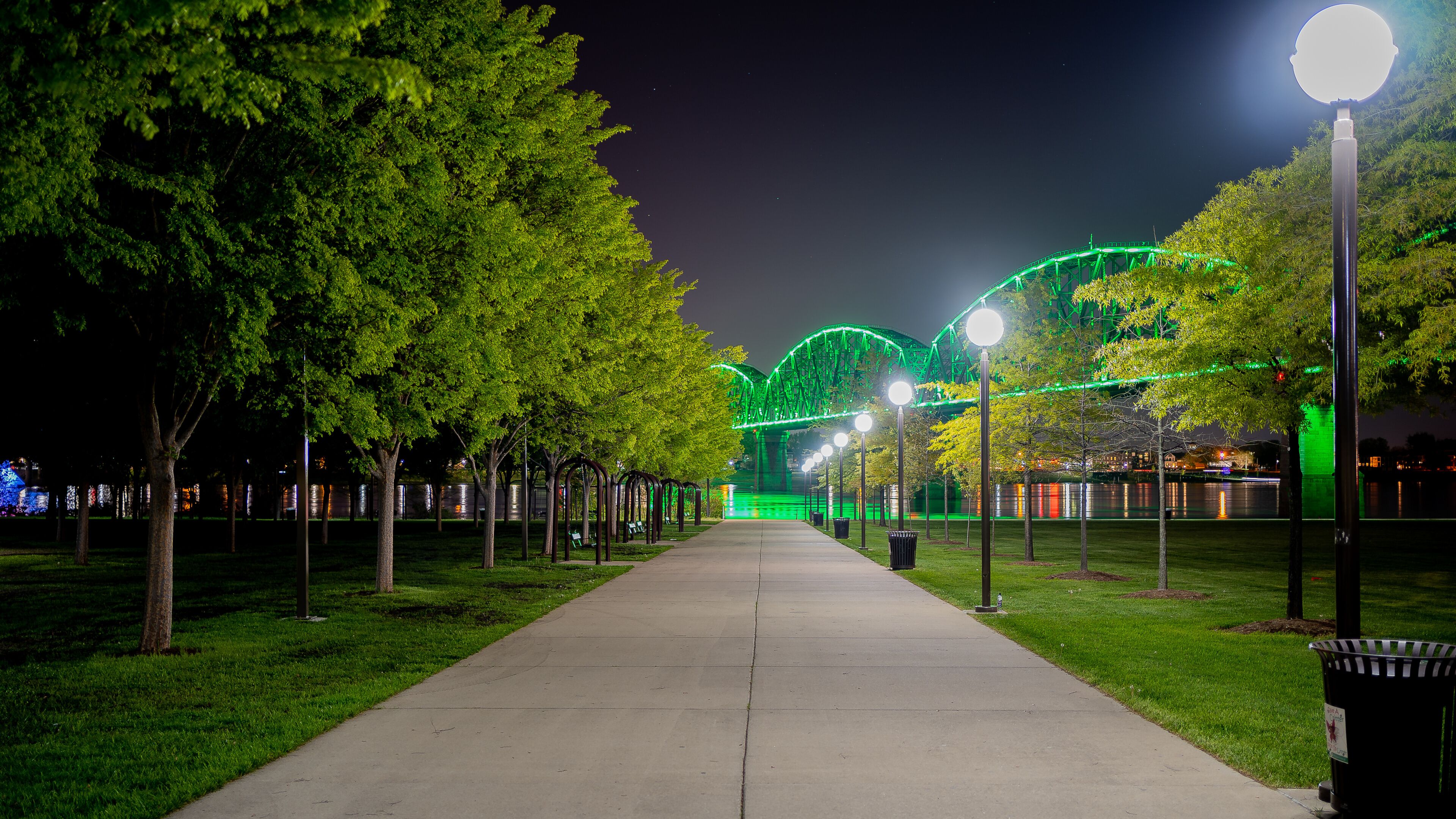 Walkway at Waterfront Park in Louisville, KY with the Big Four bridge in background lit green to mark those who have lost their lives to COVID-19.