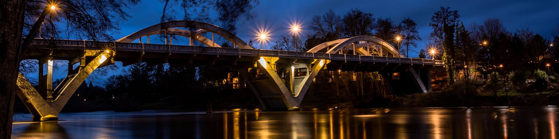 A bridge at dusk with lights reflecting on the water.