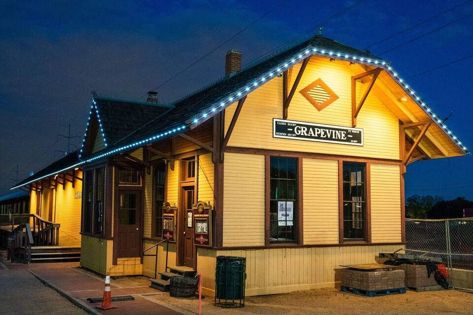 Una pequeña estación de tren iluminada llamada "GRAPEVINE", con fachada de madera y un cartel.