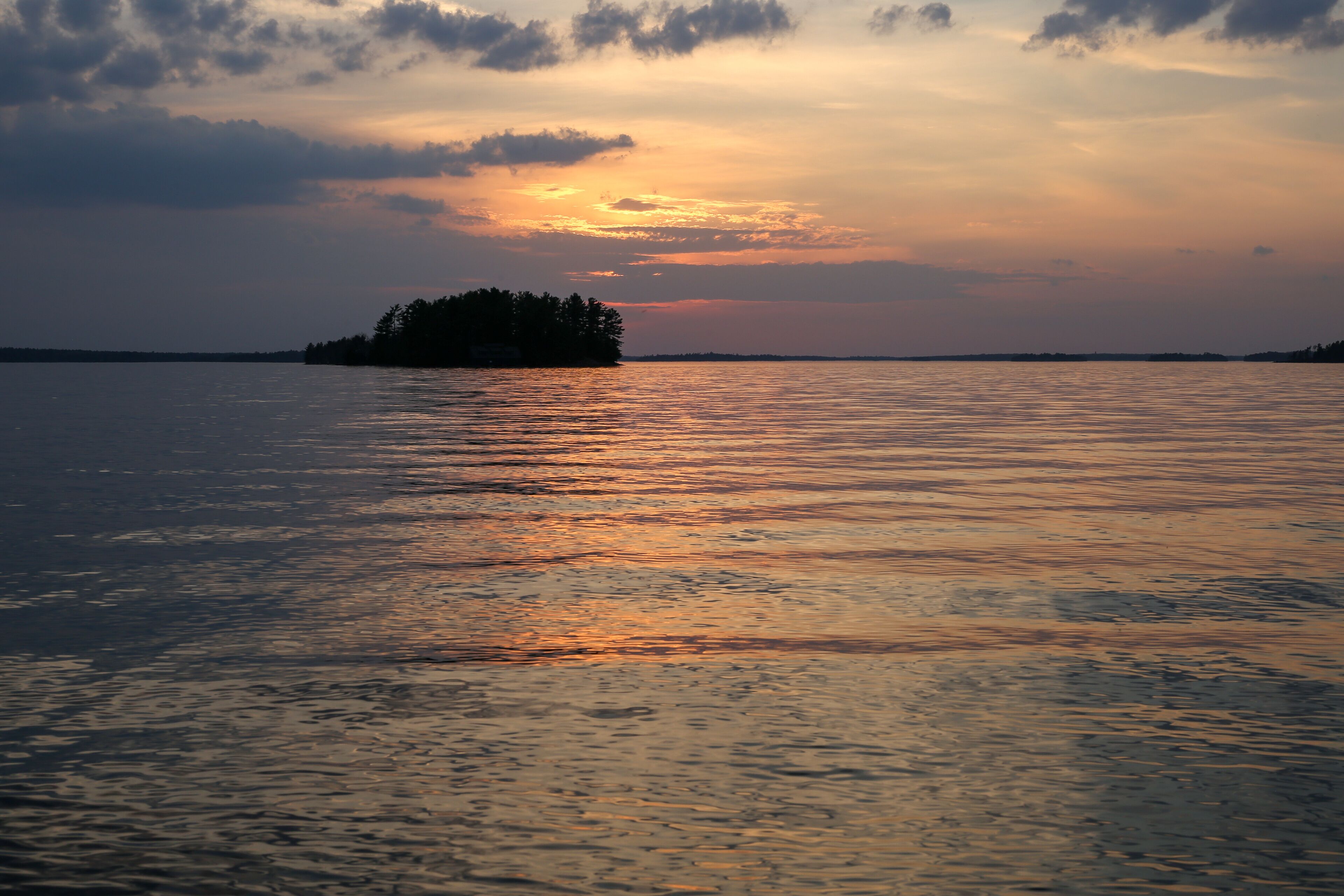Um pôr do sol sobre um lago calmo, com uma pequena ilha ao longe.