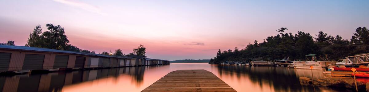 A wooden dock extending into calm waters, surrounded by trees and boats.