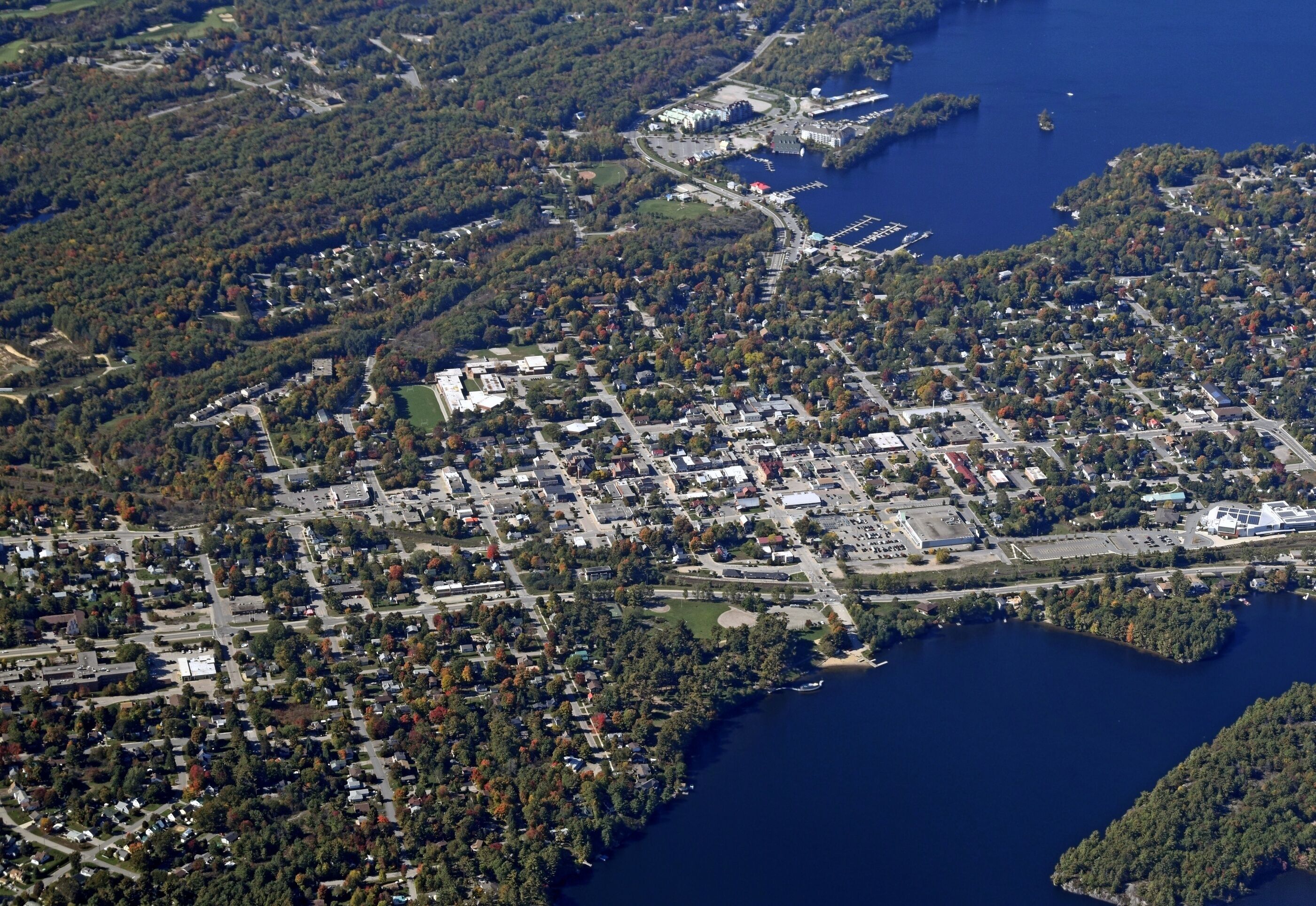 An aerial view of a town with a dense cluster of buildings, a marina, and a large body of water.