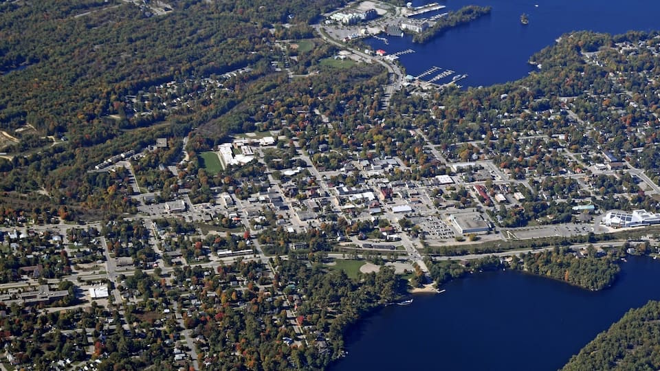An aerial view of a town with a dense cluster of buildings, a marina, and a large body of water.