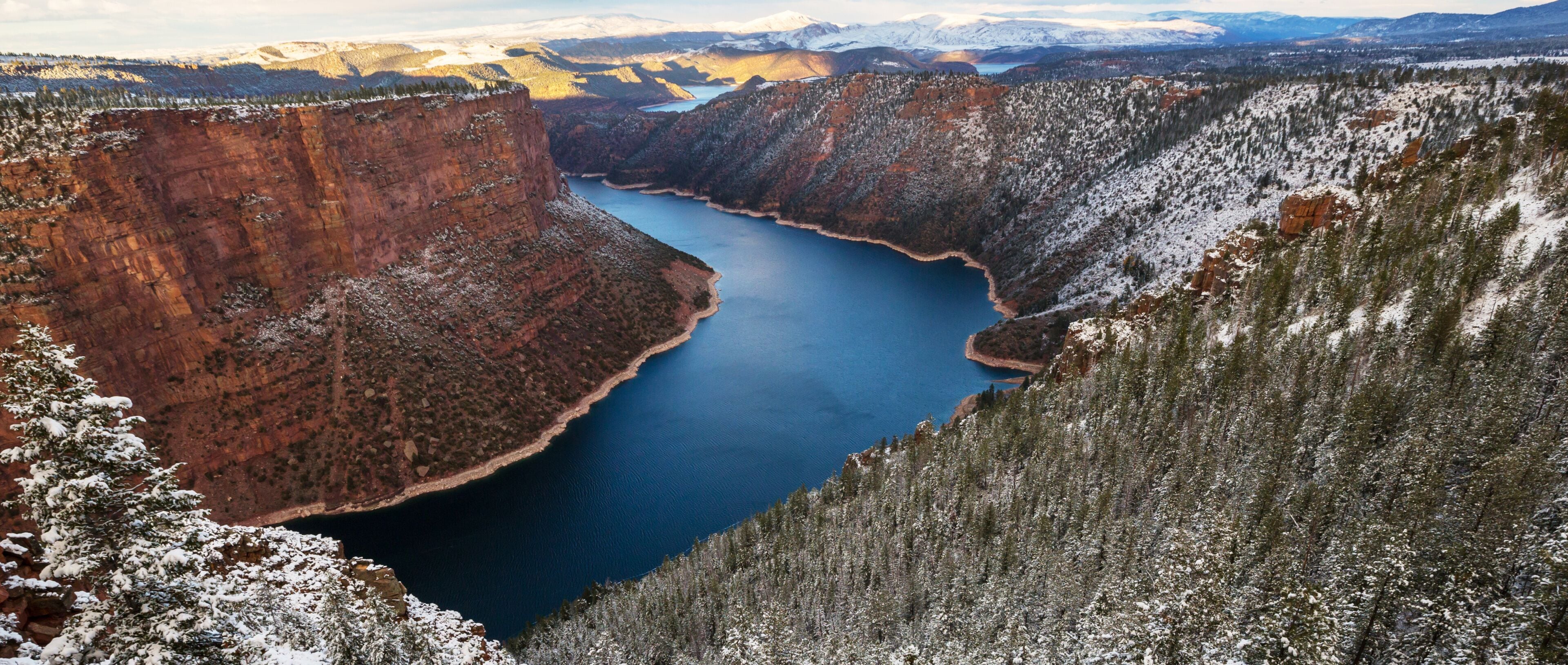 Un canyon profond, traversé par une rivière, entouré de montagnes enneigées et d’une végétation clairsemée.