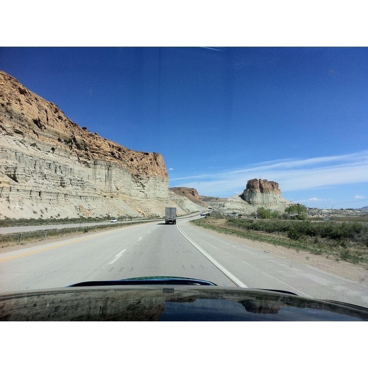 A highway with a truck in the center, flanked by steep cliffs and a prominent rock formation.
