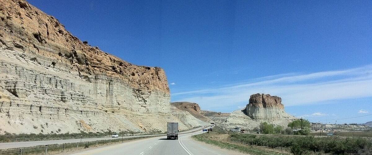 A highway with a truck in the center, flanked by steep cliffs and a prominent rock formation.