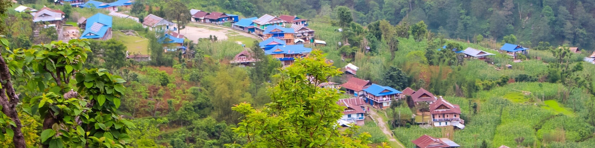 Un pueblo situado en un valle exuberante, con campos en terrazas y casas con tejados azules.