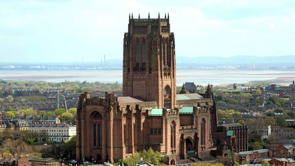 Una iglesia histórica con una alta torre y ventanas de arco, rodeada por un paisaje urbano y un río.