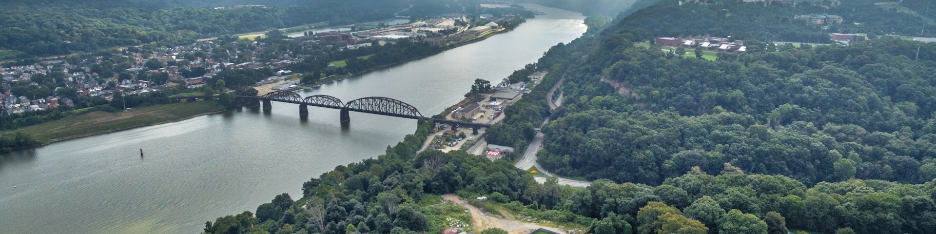 Um rio com uma ponte, rodeado por uma floresta densa e uma pequena cidade.