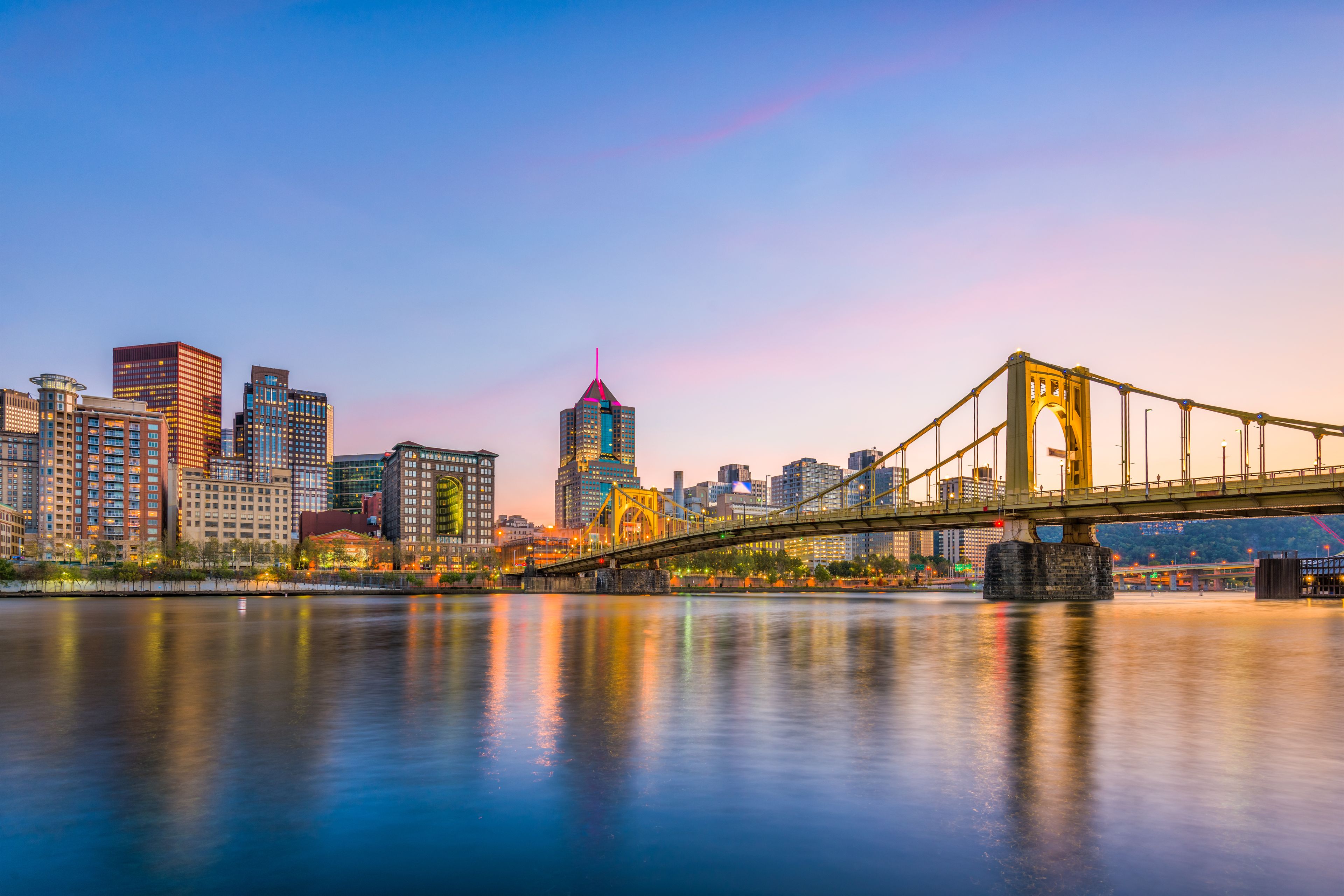 A city skyline with modern buildings and a prominent bridge spanning a river.