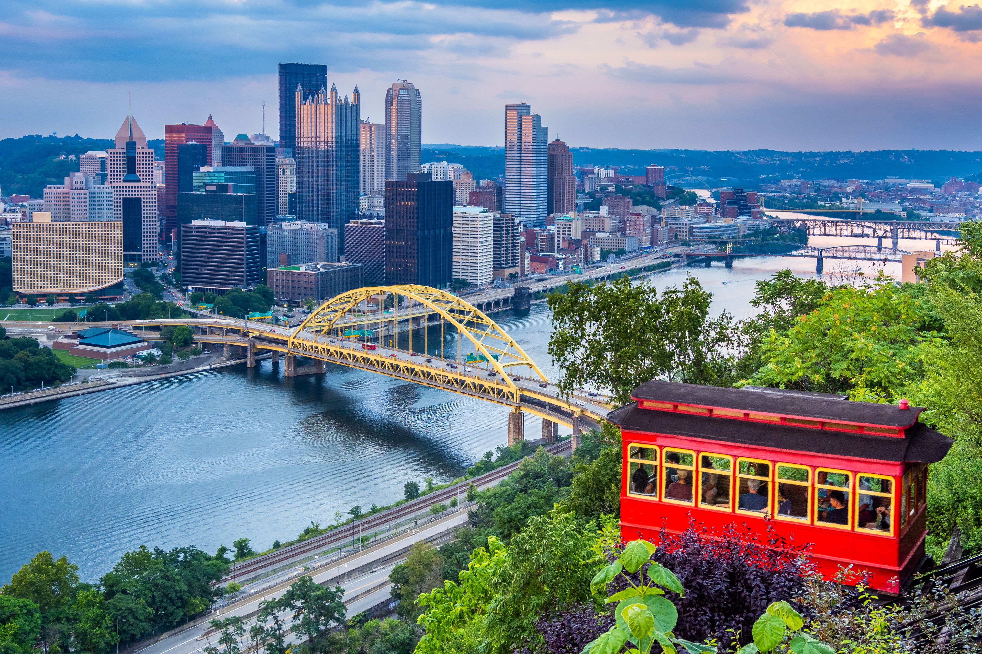 A cityscape with a prominent yellow bridge over a river, a red trolley, and a skyline of modern buildings.