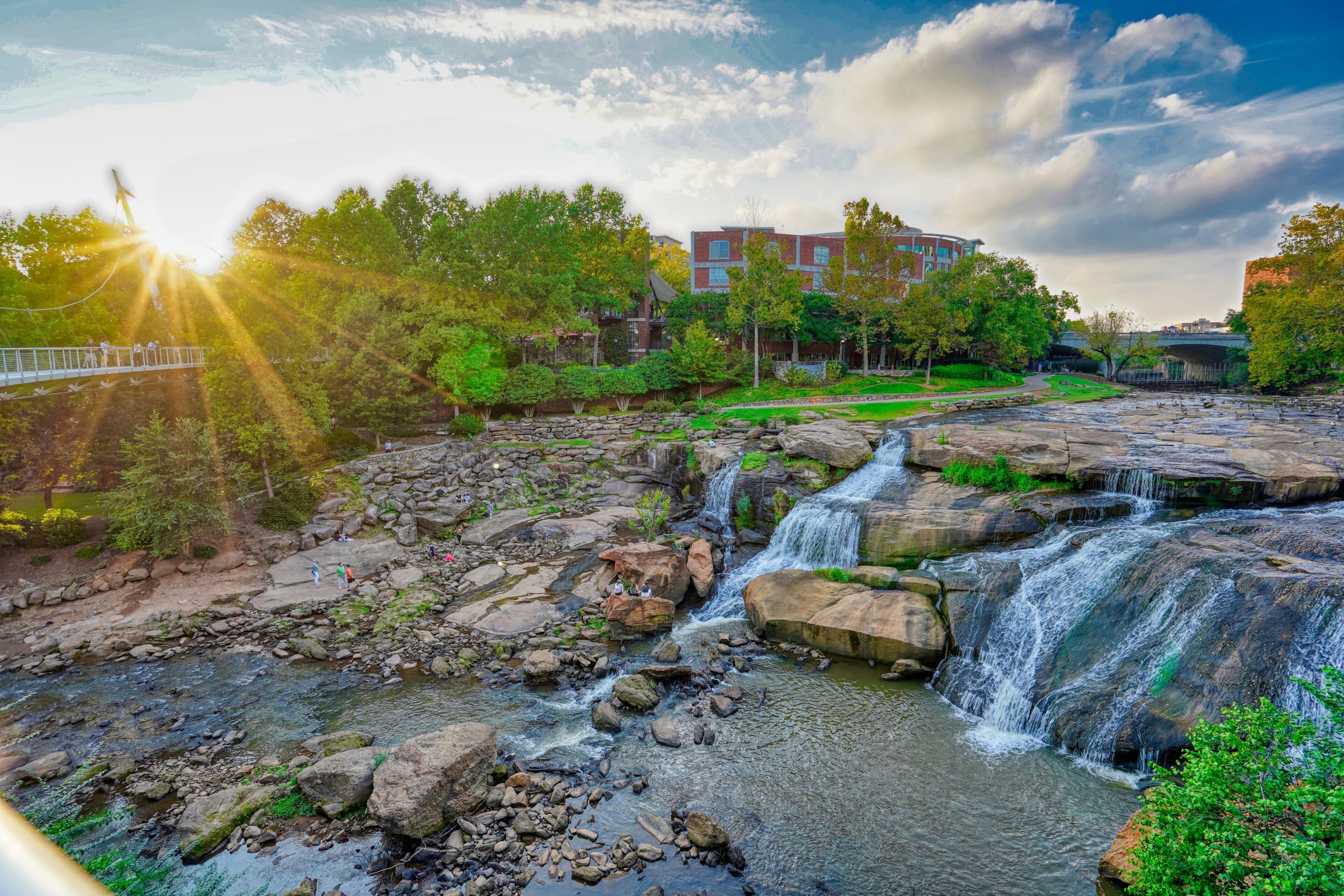 Una cascada que se precipita sobre rocas, un puente y un edificio al fondo.