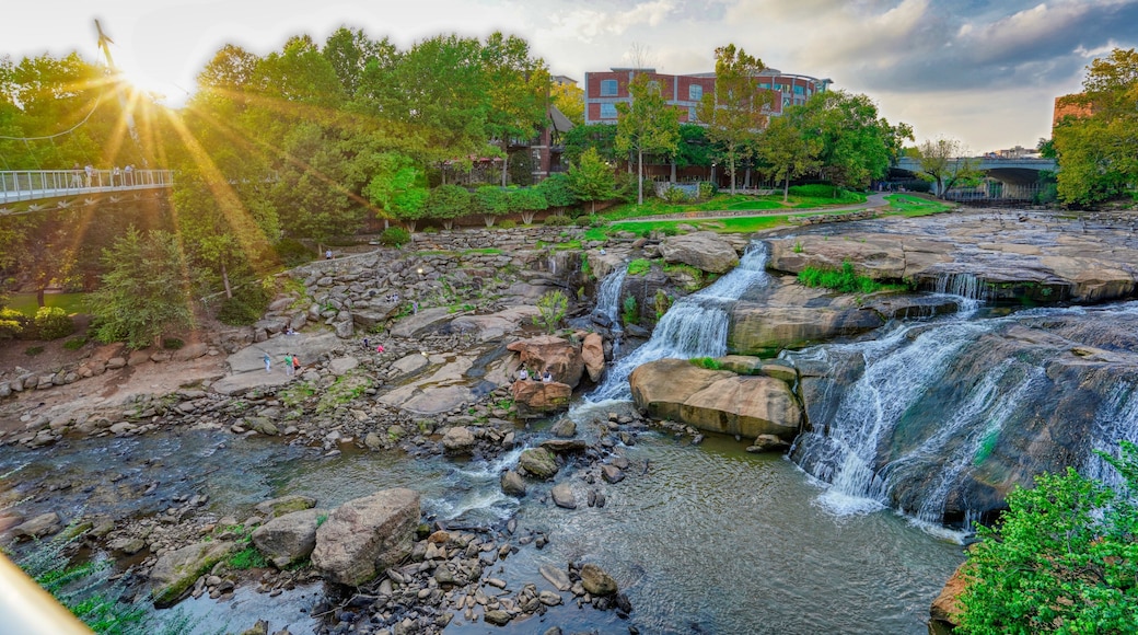 Una cascada que se precipita sobre rocas, un puente y un edificio al fondo.