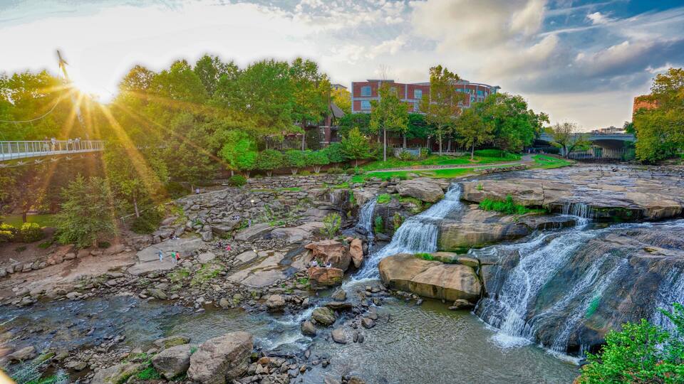 A waterfall cascading over rocks, a bridge, and a building in the background.