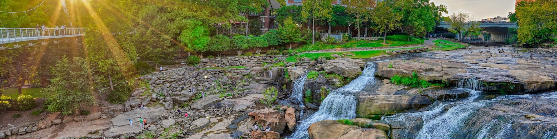 Una cascada que se precipita sobre rocas, un puente y un edificio al fondo.