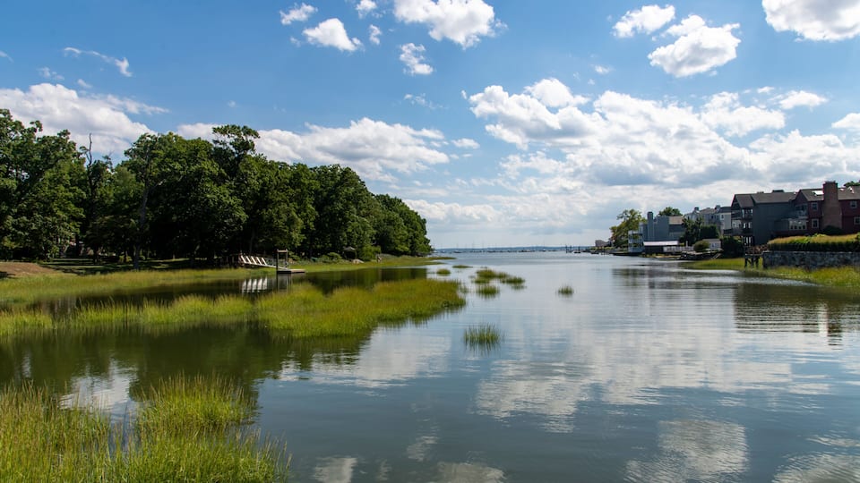 View over the tranquil water of Smith Cove in Greenwich, CT, USA with view towards the Long Island sound and large cumulus clouds in blue sky reflected in water