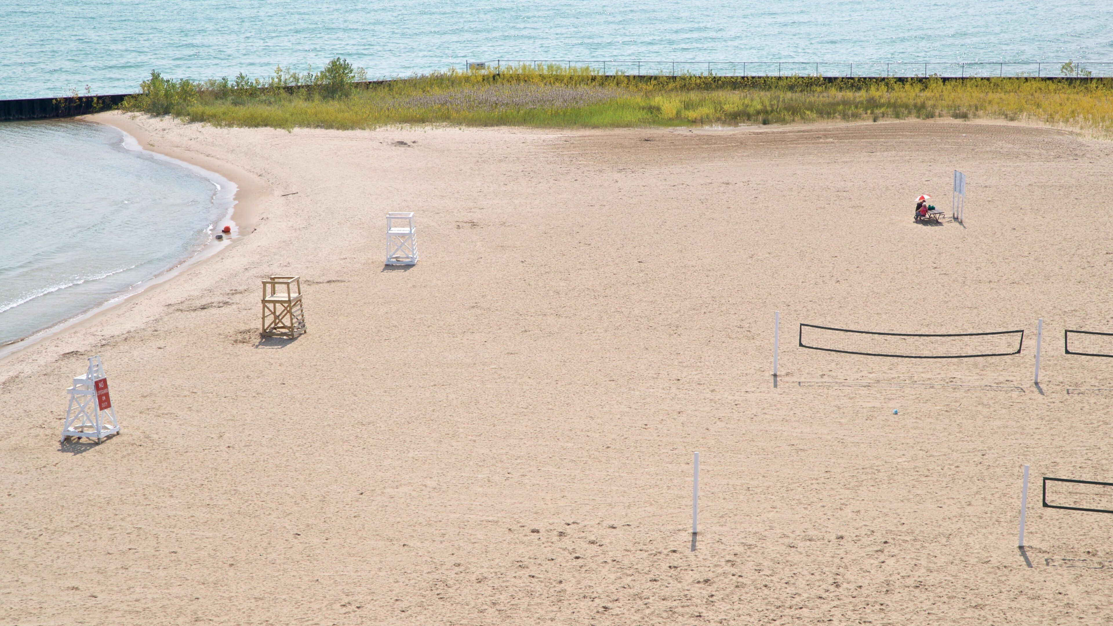 A sandy beach with lifeguard chairs, a volleyball net, and a no swimming sign.