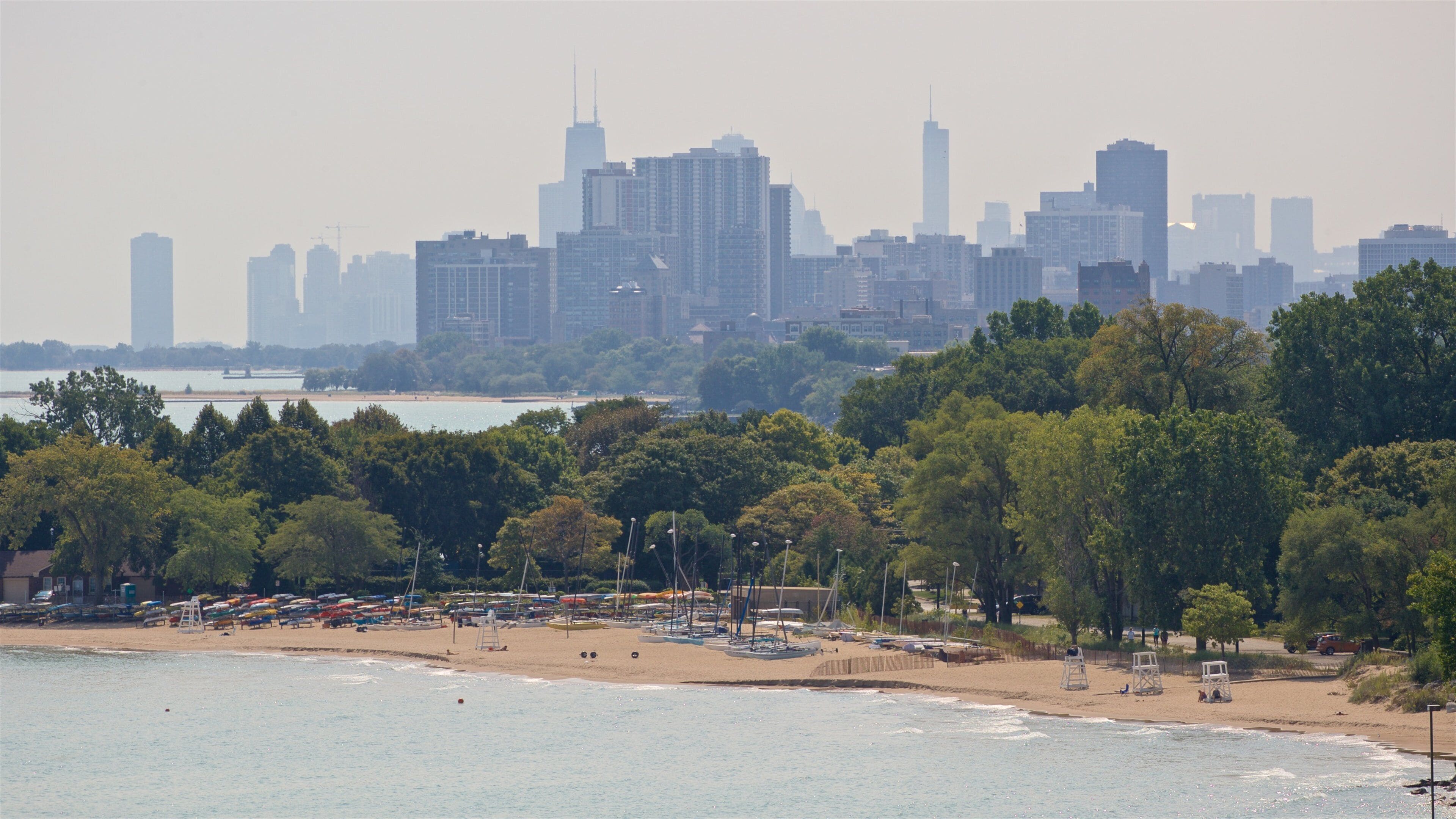 A beach with umbrellas and a city skyline in the background.
