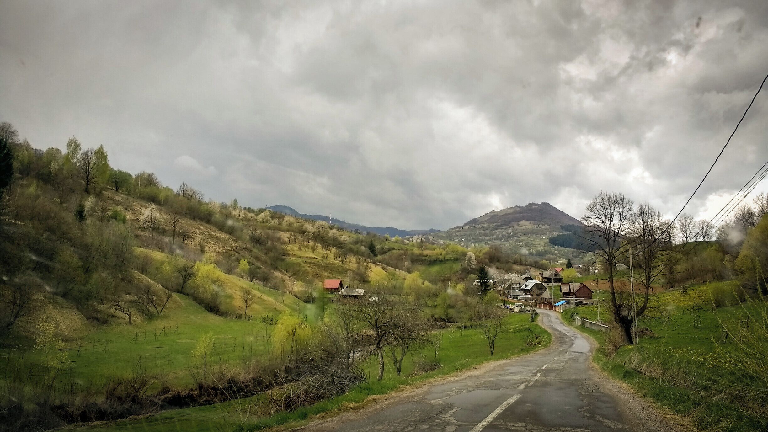 A rural road winding through a hilly landscape with scattered houses and a mountain in the background.