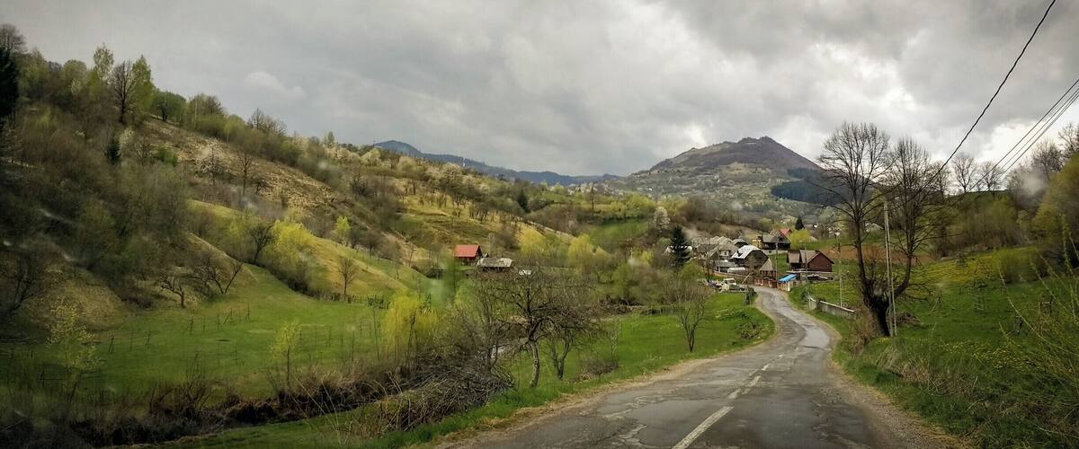 A rural road winding through a hilly landscape with scattered houses and a mountain in the background.
