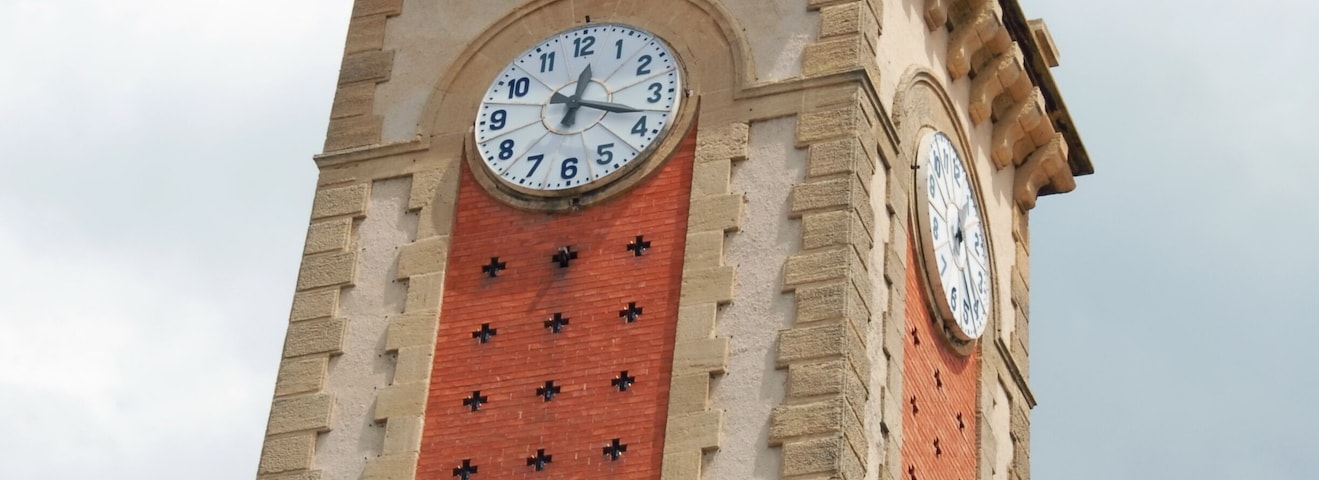 Un campanario con veleta, que presenta una esfera del reloj y una fachada de ladrillo rojo.