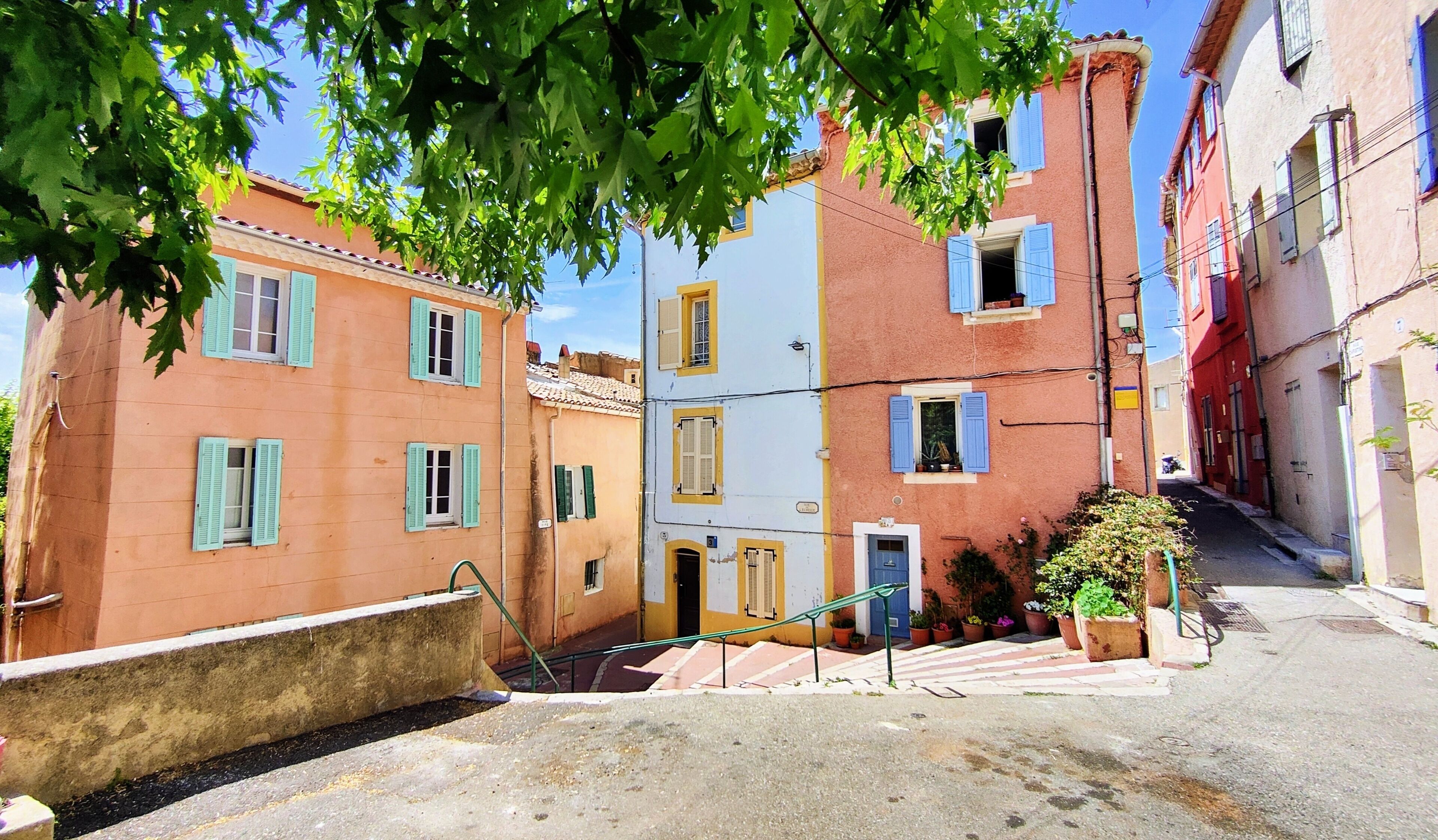 A narrow street with colorful buildings, a staircase, and a tree with green leaves.