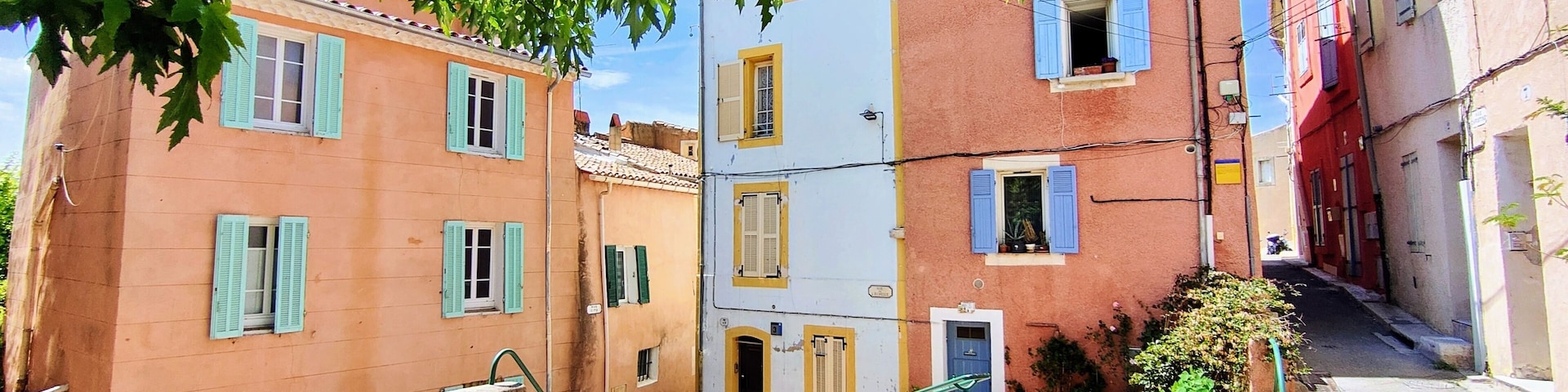 A narrow street with colorful buildings, a staircase, and a tree with green leaves.