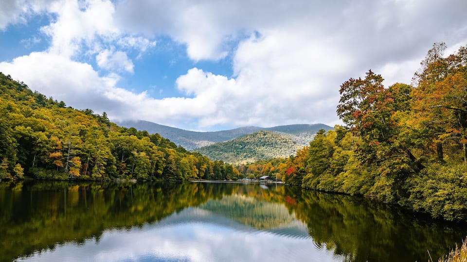 A calm lake surrounded by autumn-colored trees and hills.