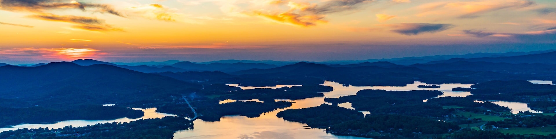 Un atardecer sobre un paisaje montañoso con múltiples lagos y densos bosques.