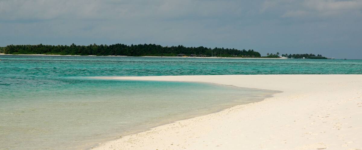 A beach with clear turquoise water and white sand, surrounded by a forested island.