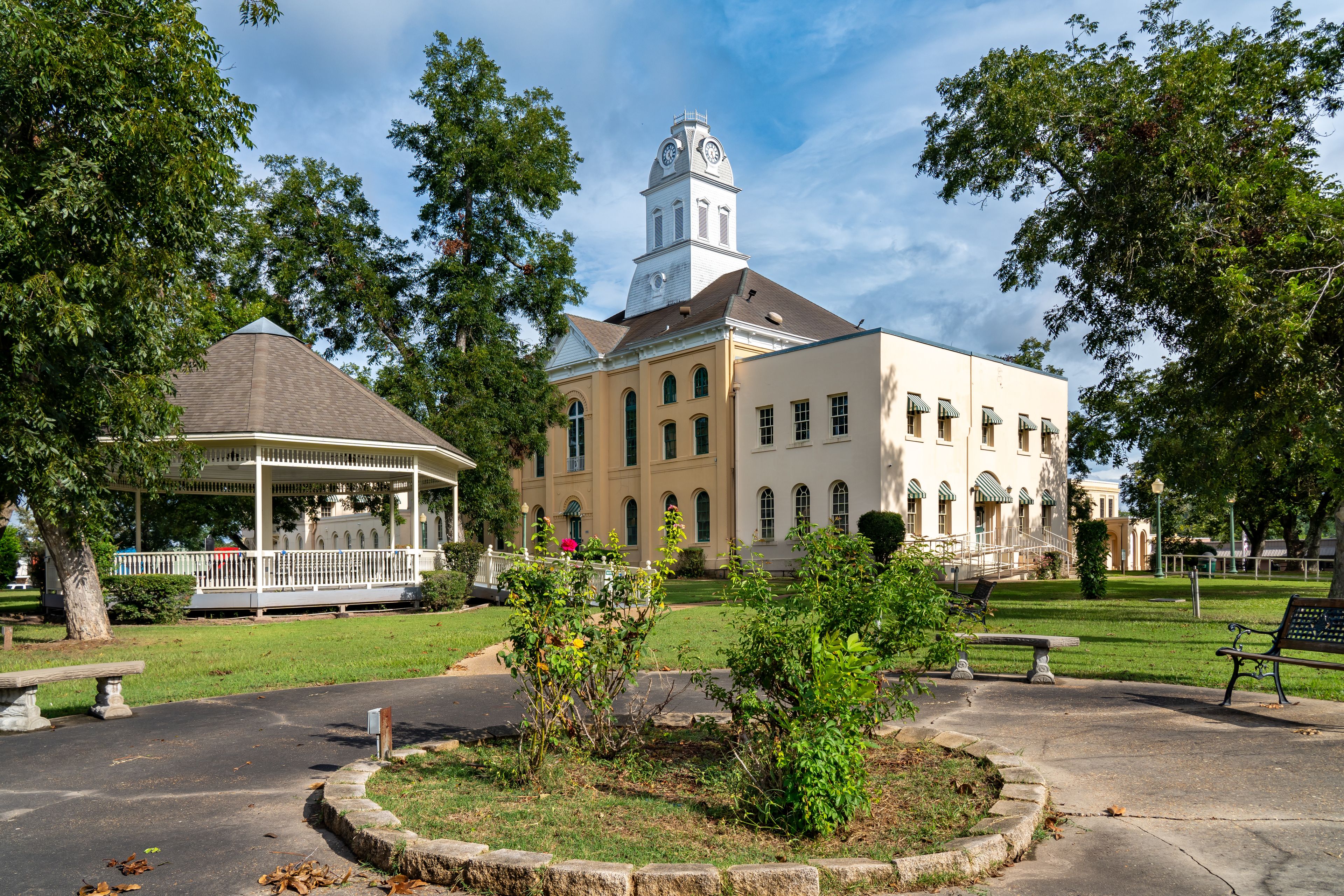 A historic building with a clock tower, a gazebo, and a well-maintained lawn.