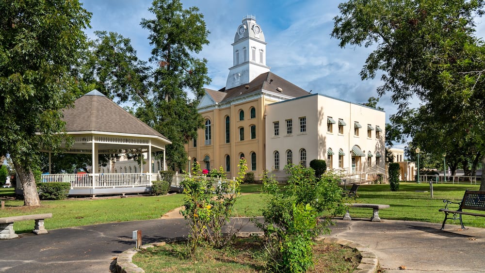 A historic building with a clock tower, a gazebo, and a well-maintained lawn.