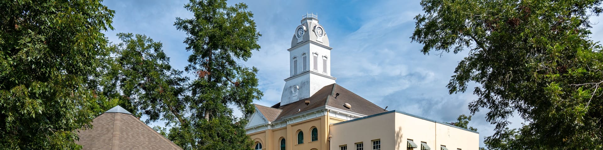A historic building with a clock tower, a gazebo, and a well-maintained lawn.