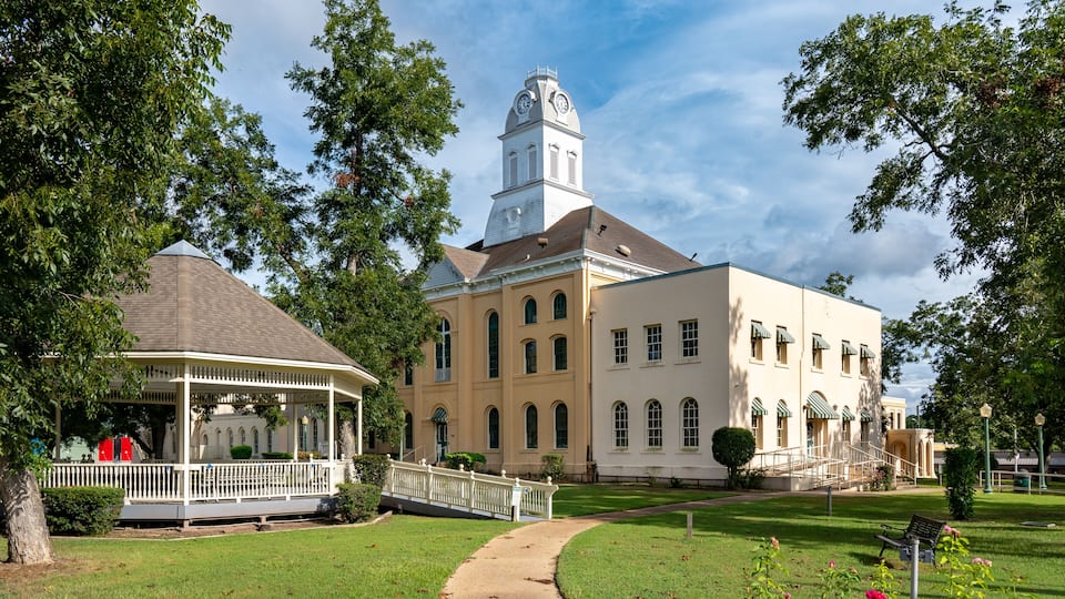 A historic building with a clock tower, a gazebo, and a well-maintained lawn.