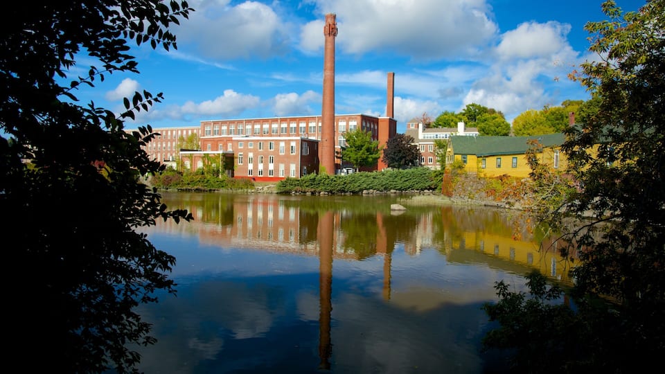 A river reflecting buildings, including a red brick factory and a yellow house.