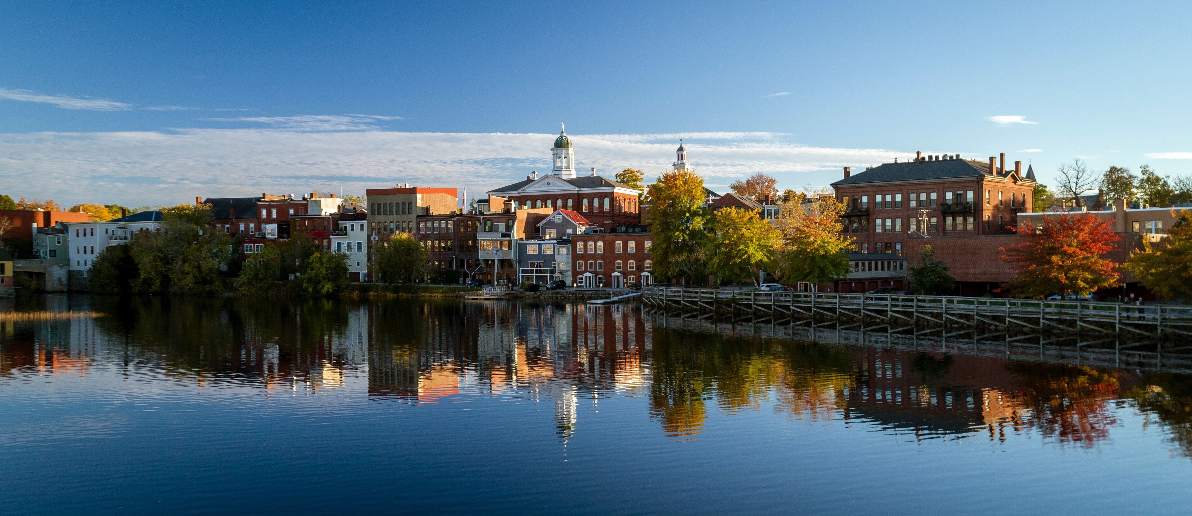 A calm river reflecting buildings and trees.