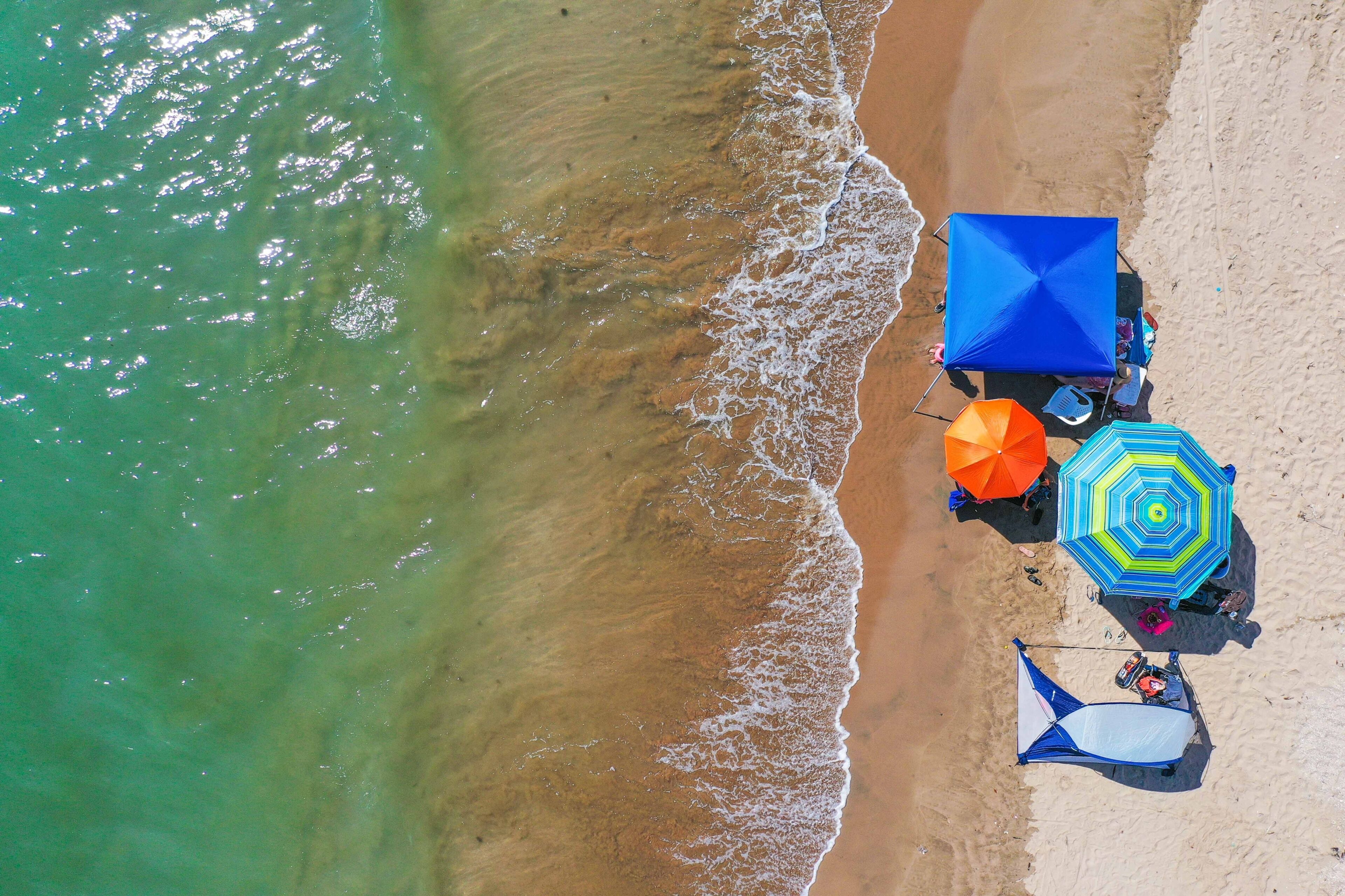 A beach with a blue umbrella, a multicolored umbrella, and a white canopy.