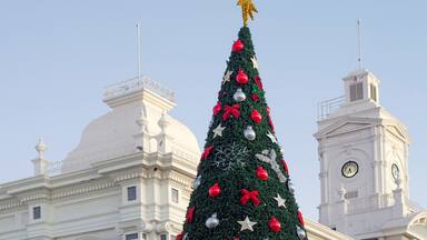 A large Christmas tree with red and silver ornaments, a golden star on top, and a clock tower in the background.