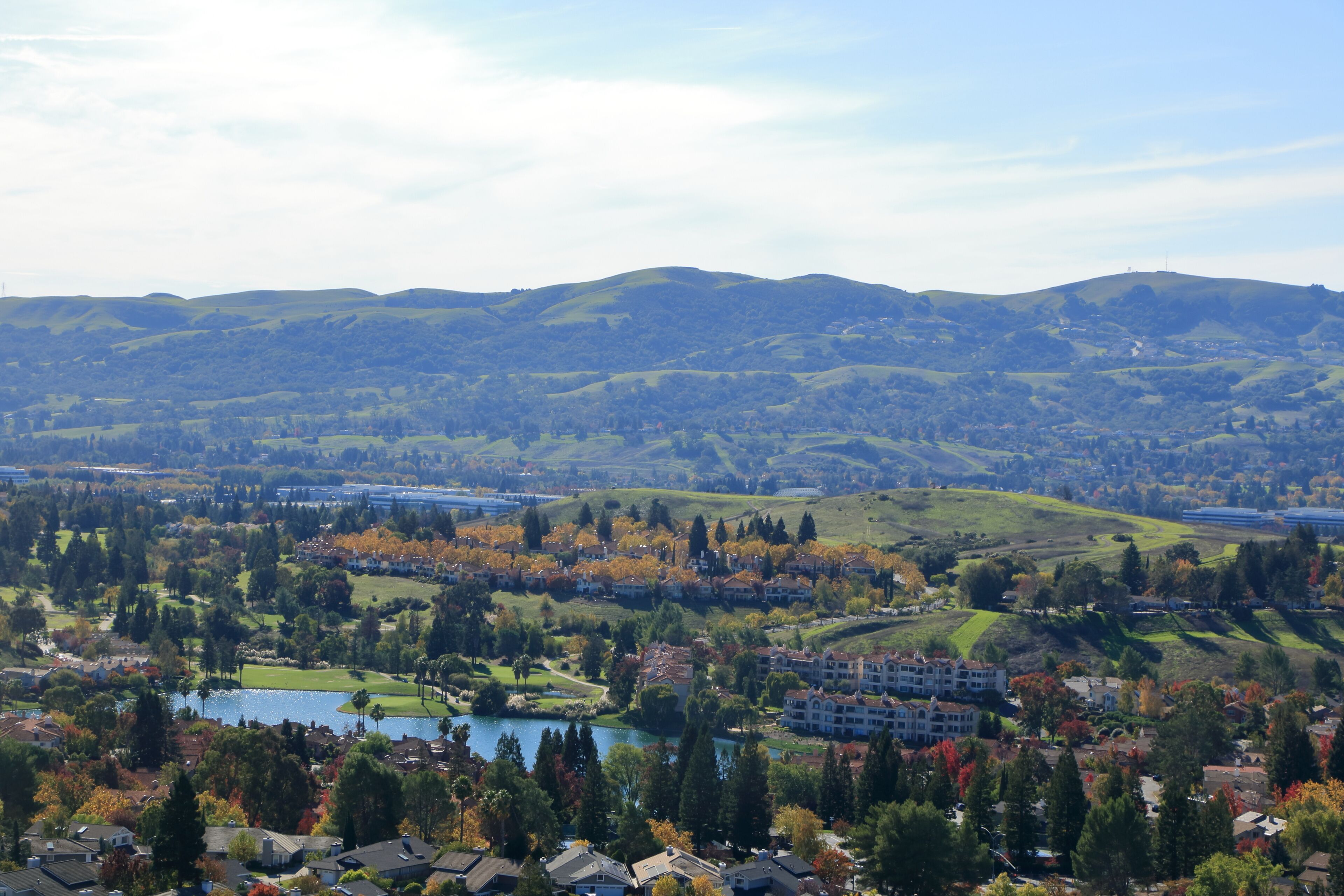 A panoramic view of a hilly landscape with a lake, residential areas, and autumn-colored trees.