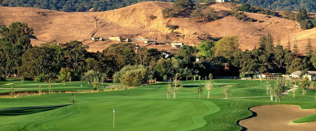 A golf course with a backdrop of hills and scattered houses.