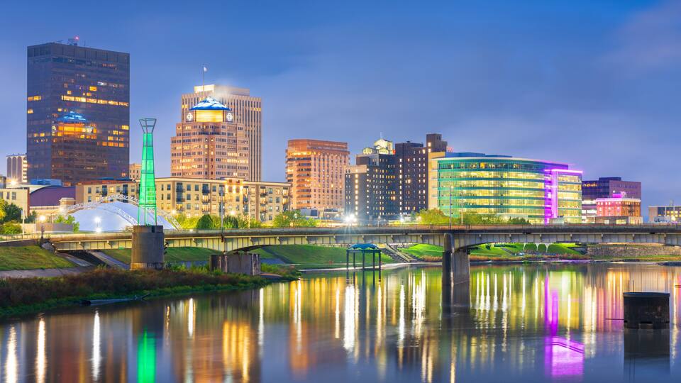 A city skyline with illuminated buildings reflecting on a calm river.